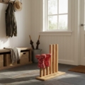 A personalized wooden boot rack sits on a slate-tiled floor in a sunlit farmhouse mudroom. The rack features four vertical pegs of varying heights; the two shorter front pegs hold a pair of small red wellington boots with white polka dots, stored upside down. The two taller rear pegs are empty, showcasing the natural wood grain. In the background, a rustic wooden bench with wicker storage baskets sits below a wall-mounted coat rack holding a jacket and a sunhat. A large window and a white door allow soft, natural light to fill the room, highlighting the 'Rita's Mucky Boots' engraving on the base of the rack.