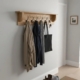 Wall-mounted wooden coat rack with shelf and hooks in a bright, modern entryway, styled with coats and accessories.